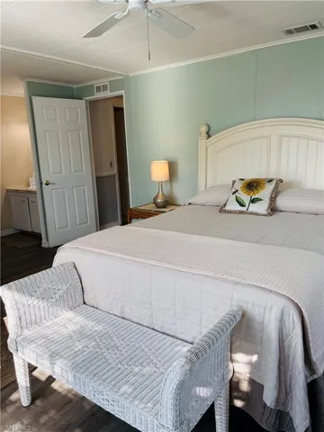 Bedroom with wood finished floors, a decorative wall, crown molding, and a ceiling fan