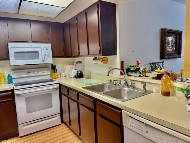 Kitchen with white appliances, dark brown cabinetry, and light countertops