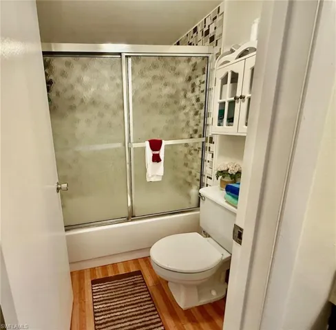 Bathroom with combined bath / shower with glass door and wood finished floors