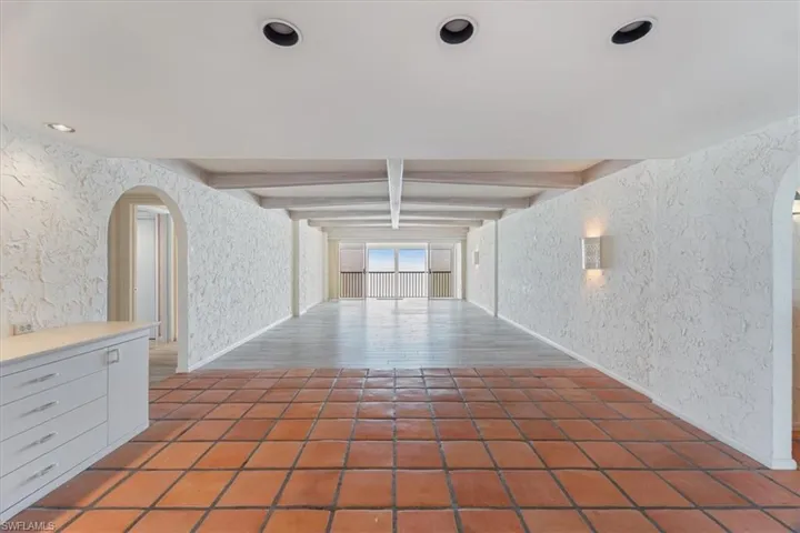 Hallway with arched walkways, wallpapered walls, beam ceiling, and tile patterned flooring
