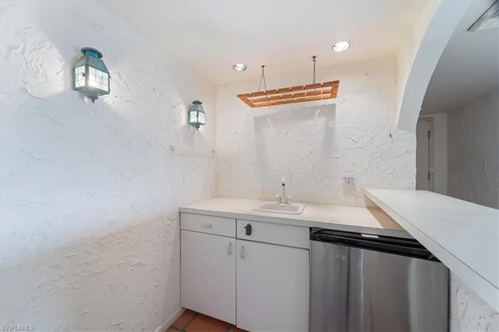 Kitchen featuring a textured wall, light countertops, white cabinetry, stainless steel dishwasher, and recessed lighting