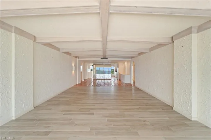 Hallway with a textured wall, wood tiled floors, and beamed ceiling
