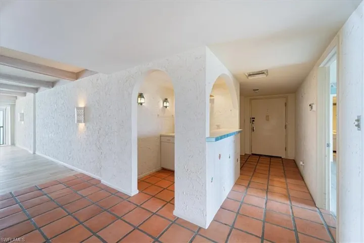 Hallway with arched walkways, light tile patterned floors, wallpapered walls, and beam ceiling
