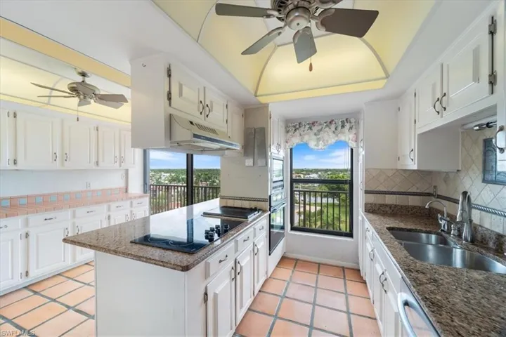 Kitchen featuring a ceiling fan, a raised ceiling, white cabinetry, and under cabinet range hood