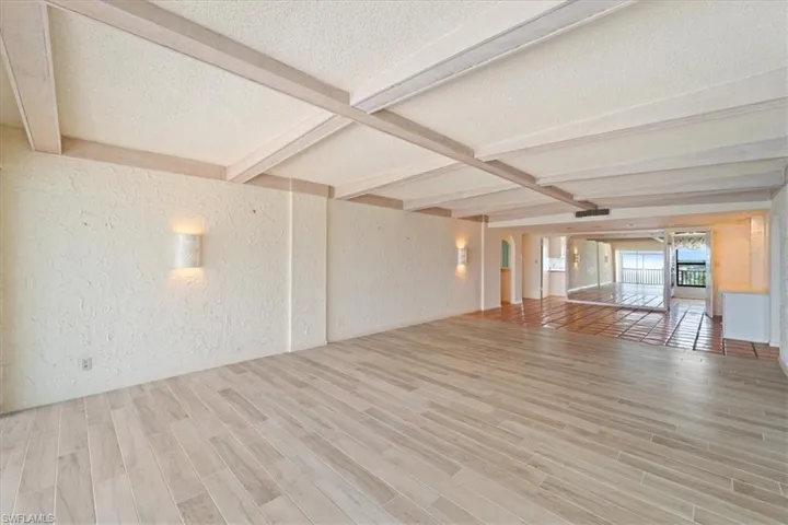Unfurnished living room featuring a textured wall, a textured ceiling, beam ceiling, and light wood-style floors