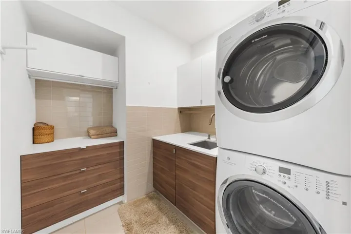 Laundry room with light tile patterned floors, cabinet space, stacked washer / drying machine, and tile walls
