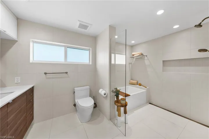 Bathroom with tile walls, a bathtub, light tile patterned floors, a walk in shower, and vanity