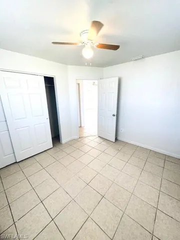 Neutral-toned tile flooring, white walls, and a ceiling fan with integrated lighting