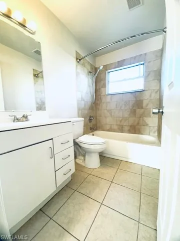 Spacious bathroom featuring a white vanity with ample storage, ceramic tile flooring, and a tub/shower combination with curved glass enclosure and natural window lighting