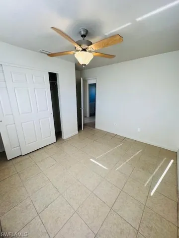 Neutral wall color, tiled flooring, ceiling fan with light fixture, and bifold closet doors