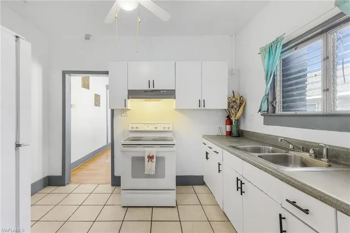 Kitchen with ceiling fan, white cabinetry, light tile patterned floors, sink, and white appliances
