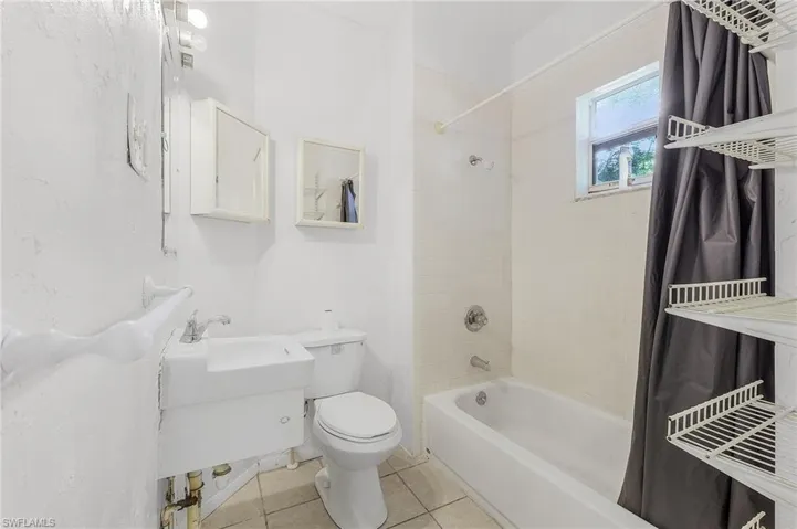 Bathroom with tile patterned floors, shower / bathtub combination with curtain, and toilet