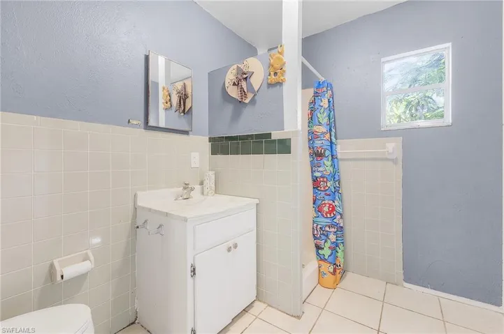 Bathroom featuring tile patterned floors, toilet, vanity, and tile walls