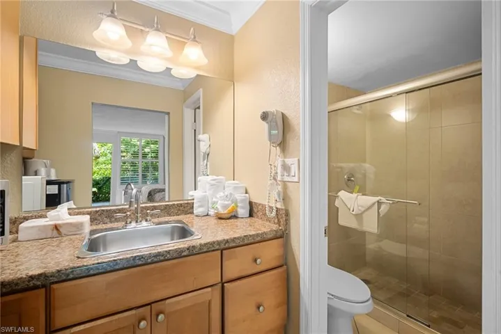 Bathroom featuring toilet, vanity, a shower with shower door, and ornamental molding