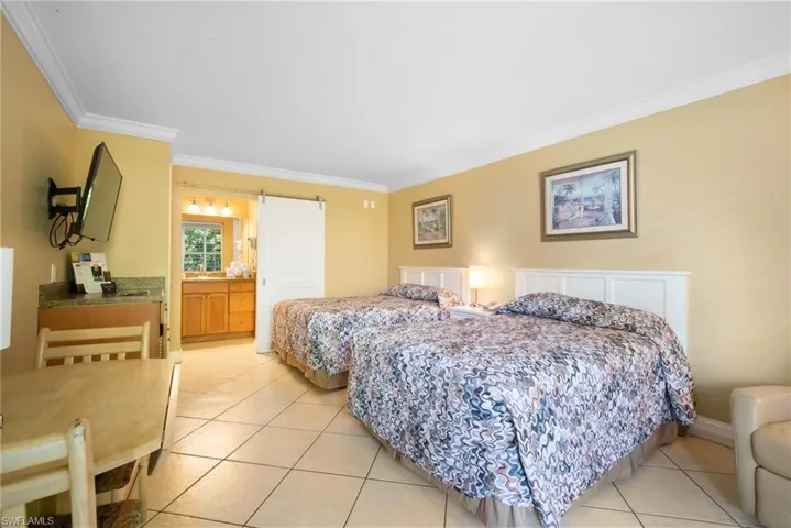 Bedroom featuring light tile patterned flooring, a barn door, ornamental molding, and ensuite bath