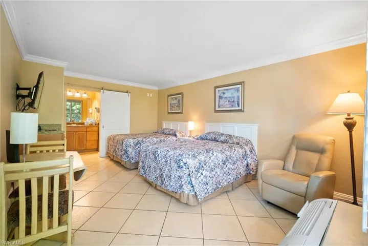 Tiled bedroom with connected bathroom, a barn door, and crown molding