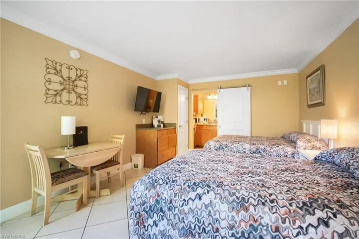 Bedroom featuring ensuite bathroom, light tile patterned flooring, and ornamental molding