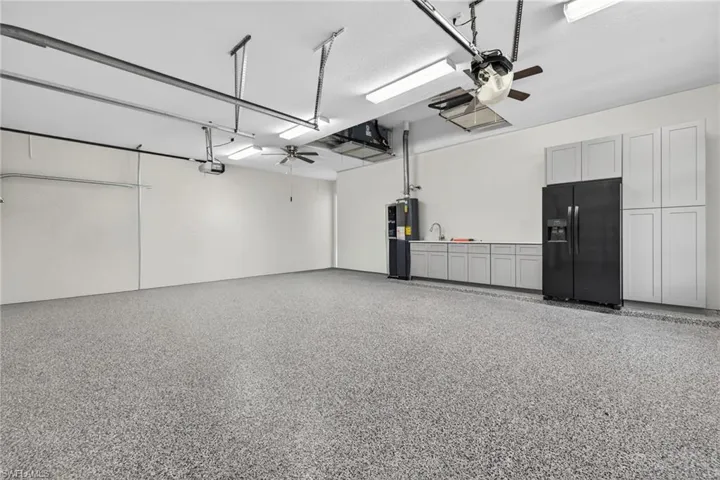 Garage with a ceiling fan, black refrigerator with ice dispenser, and water heater