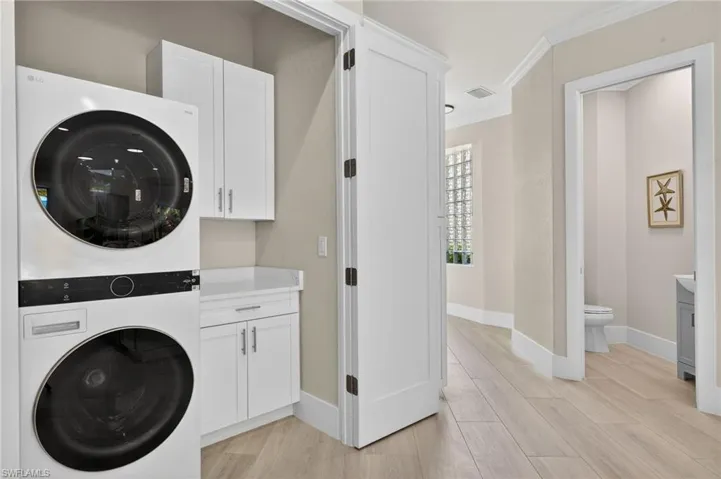 Laundry room with crown molding, stacked washer and clothes dryer, light wood-type flooring, and cabinet space