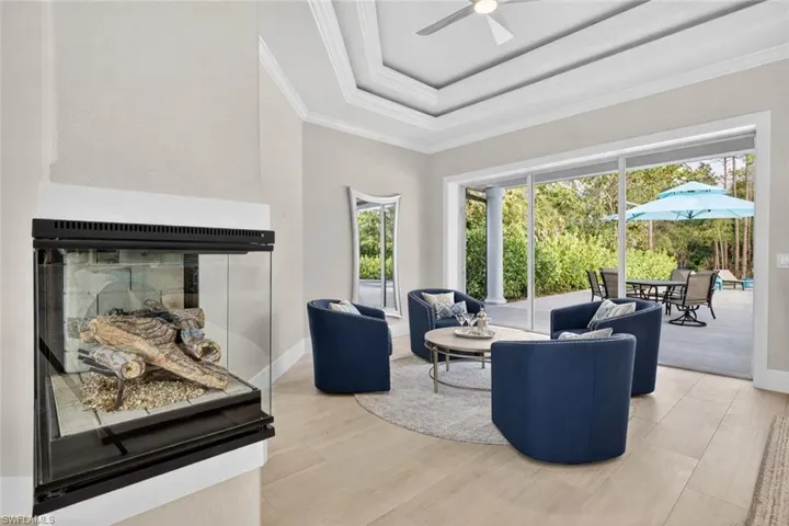 Living room with a tray ceiling, wood finished floors, a ceiling fan, ornamental molding, and a glass covered fireplace