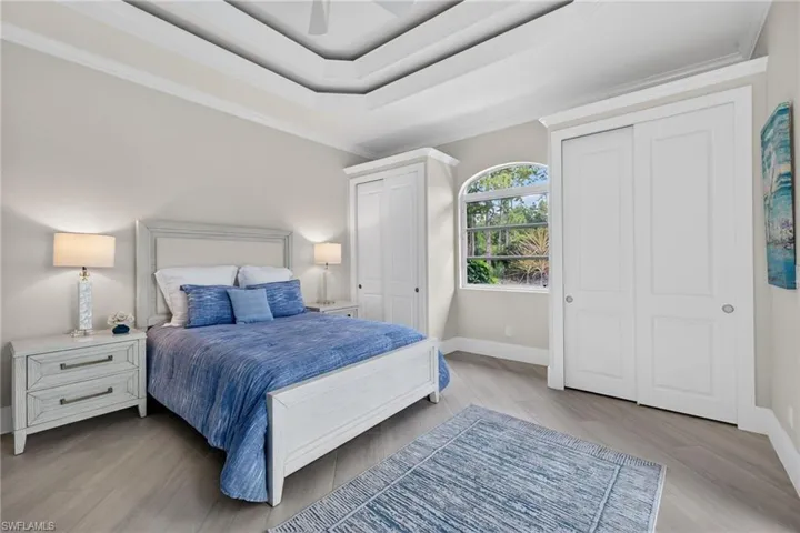 Bedroom with multiple closets, ornamental molding, light wood finished floors, a raised ceiling, and a ceiling fan