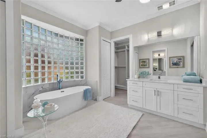 Full bath with a soaking tub, vanity, crown molding, a spacious closet, and tile walls
