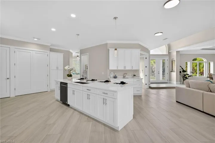 Kitchen featuring open floor plan, decorative light fixtures, white cabinets, a center island with sink, and light wood-style floors