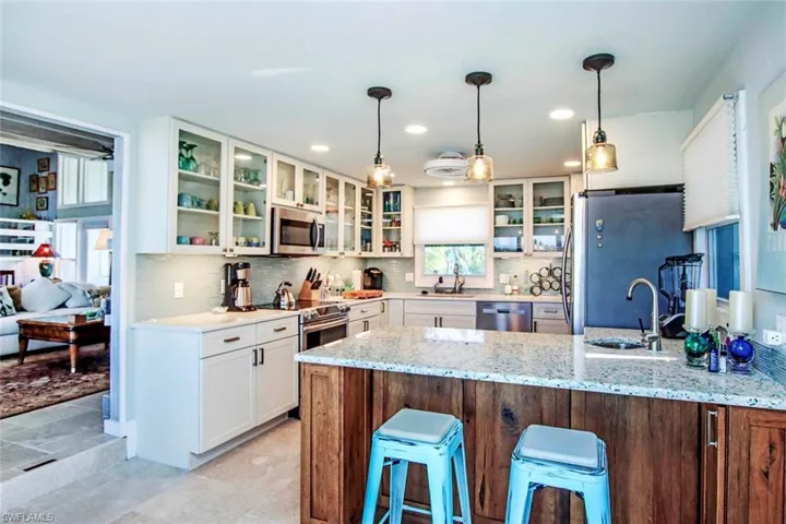 Kitchen with a breakfast bar area, decorative light fixtures, appliances with stainless steel finishes, light stone counters, and a peninsula