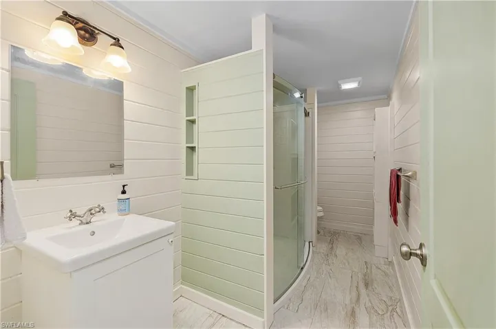 Bathroom with ornamental molding, vanity, a shower with door, toilet, and wood walls