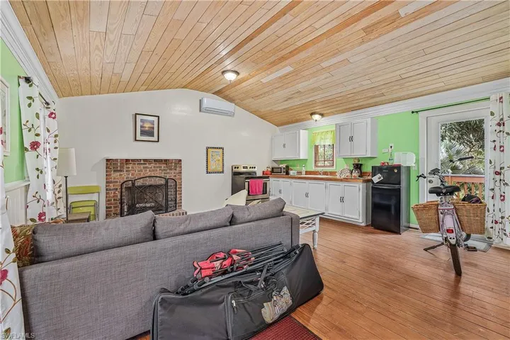 Living room featuring a brick fireplace, a wall unit AC, wooden ceiling, light hardwood / wood-style floors, and lofted ceiling