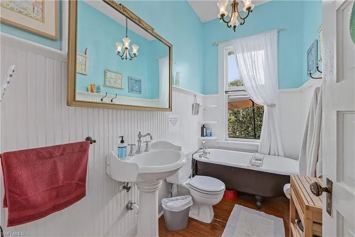 Bathroom featuring hardwood / wood-style flooring, a notable chandelier, a bathtub, and toilet