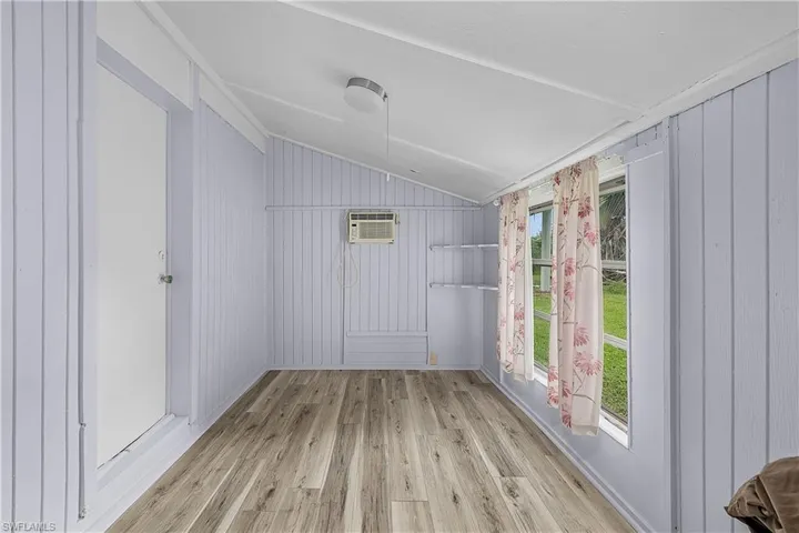 Spare room featuring an AC wall unit, wooden walls, light hardwood / wood-style floors, and lofted ceiling