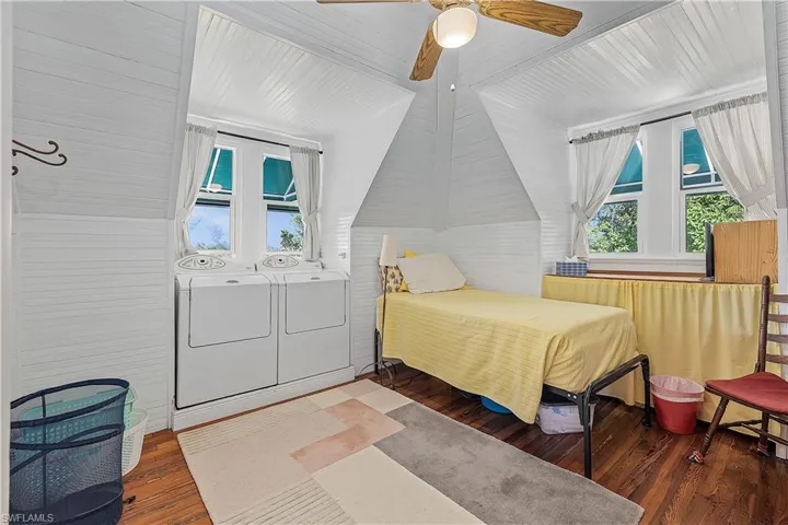 Bedroom featuring dark hardwood / wood-style floors, ceiling fan, washer and dryer, and lofted ceiling