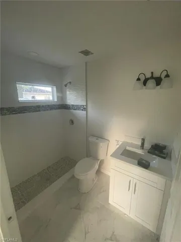 Bathroom featuring vanity, tile patterned floors, a tile shower, and toilet
