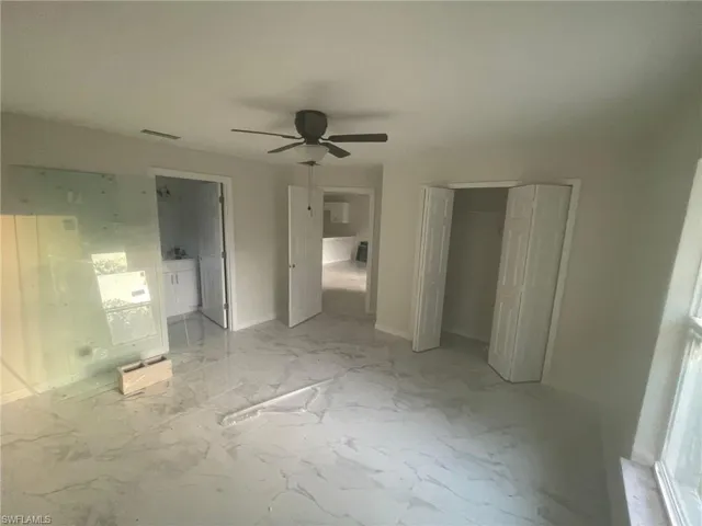 Unfurnished bedroom featuring ensuite bath, light tile patterned floors, and ceiling fan