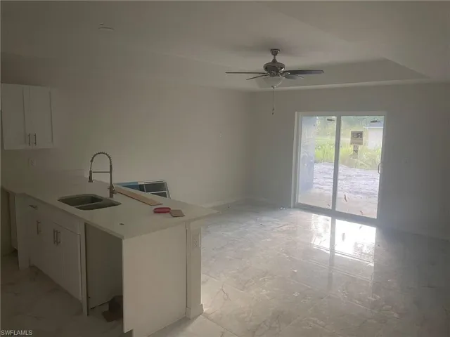 Kitchen with sink, ceiling fan, white cabinets, and light tile patterned floors