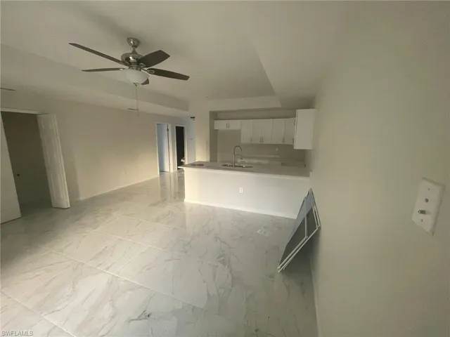 Kitchen featuring light tile patterned flooring, kitchen peninsula, white cabinets, ceiling fan, and sink