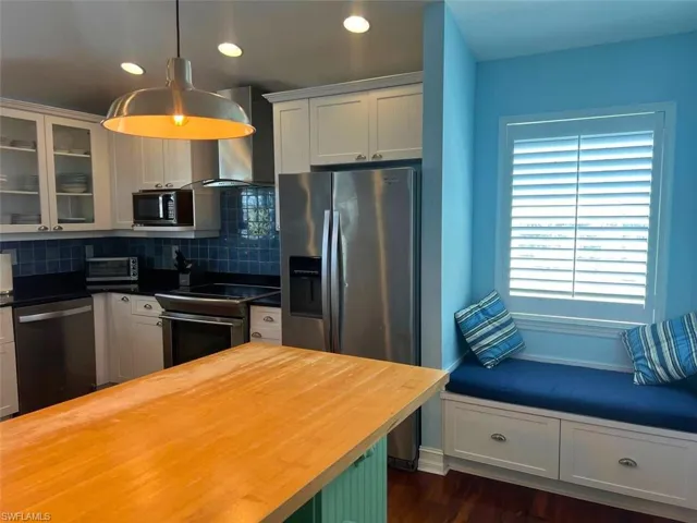 Kitchen with butcher block counters, tasteful backsplash, decorative light fixtures, appliances with stainless steel finishes, and wall chimney range hood(Photo may be virtually enhanced)