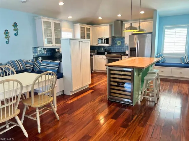 Kitchen featuring stainless steel (Photo may be virtually enhanced)appliances, white cabinets, a kitchen island, beverage cooler, and wall chimney exhaust hood