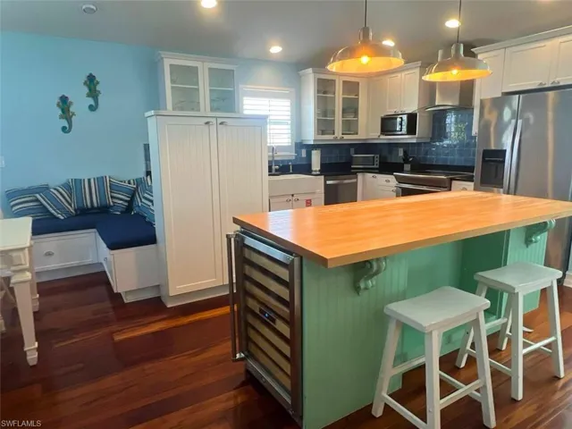 Kitchen featuring butcher block countertops, a breakfast bar, white cabinets, a kitchen island, and beverage cooler(Photo may be virtually enhanced)