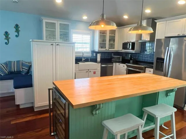 Kitchen with butcher block counters, hanging light fixtures, stainless steel appliances, a center island, and a kitchen bar (Photo may be virtually enhanced)