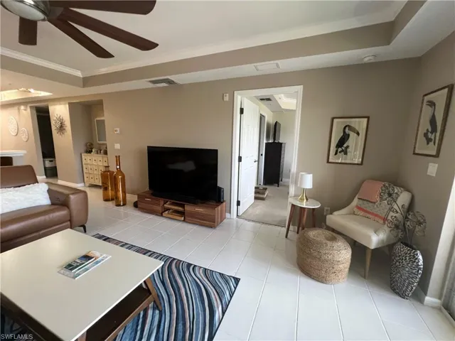Living room featuring crown molding, a tray ceiling, ceiling fan, and light tile patterned flooring
