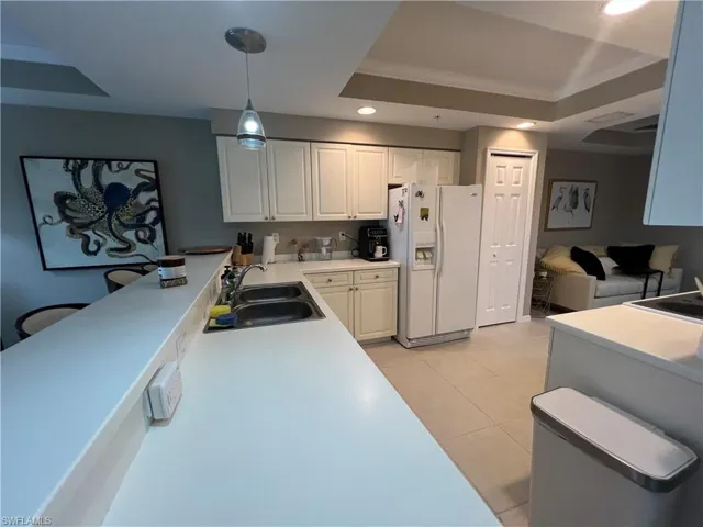 Kitchen featuring white fridge with ice dispenser, recessed lighting, ornamental molding, white cabinetry, and light tile patterned floors