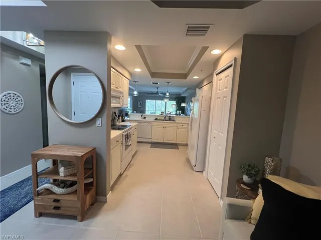 Kitchen with white appliances, light countertops, a raised ceiling, light tile patterned floors, and recessed lighting