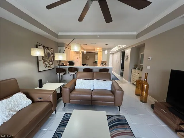 Living area featuring ornamental molding, light tile patterned floors, a ceiling fan, and a raised ceiling