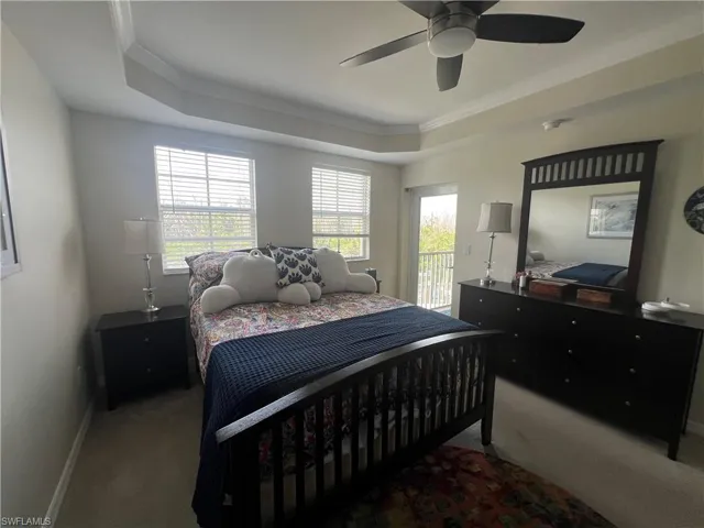 Carpeted bedroom featuring crown molding, multiple windows, a tray ceiling, access to exterior, and a ceiling fan