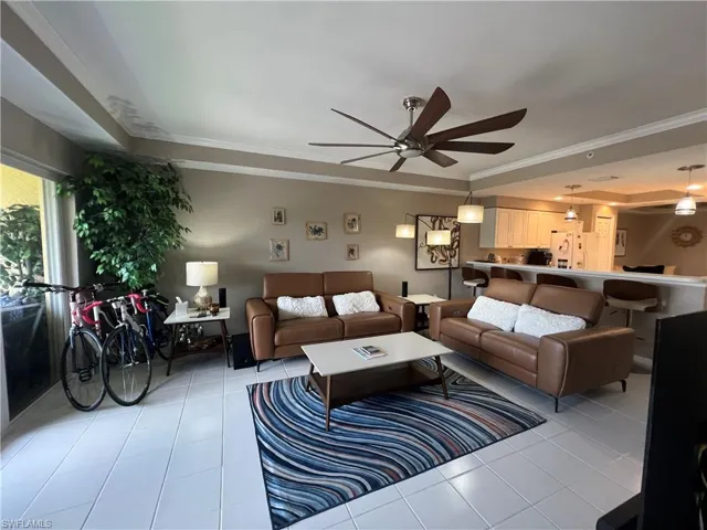Living area with a tray ceiling, ornamental molding, ceiling fan, and light tile patterned floors
