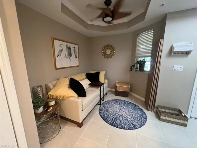 Living area featuring a tray ceiling, a ceiling fan, and light tile patterned flooring