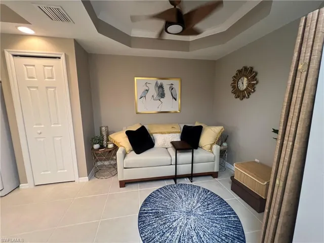 Sitting room featuring a ceiling fan, a tray ceiling, and light tile patterned flooring