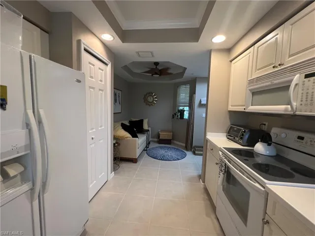 Kitchen with a tray ceiling, white appliances, recessed lighting, light countertops, and a ceiling fan